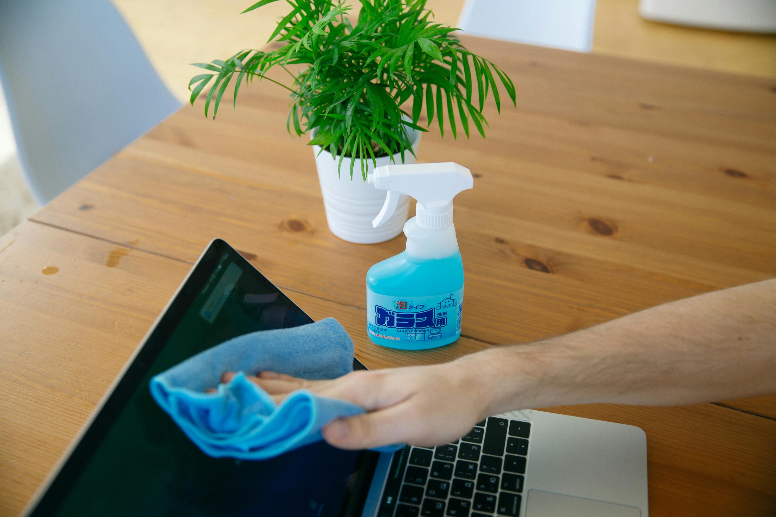 Hand wiping laptop screen with cleaner and cloth on desk in Yatala office